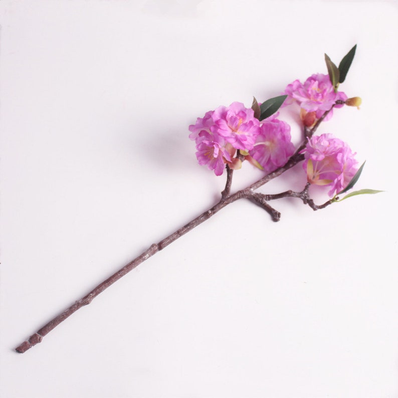 May include: A single stem of artificial pink cherry blossoms with green leaves. The stem is brown and the flowers are clustered together.