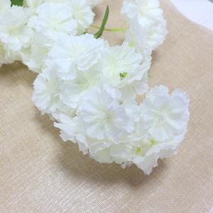 Pu&ograve; includere: Un mazzo di fiori artificiali bianchi con una texture delicata e a strati. I fiori sono disposti a cascata, creando un aspetto morbido e romantico.