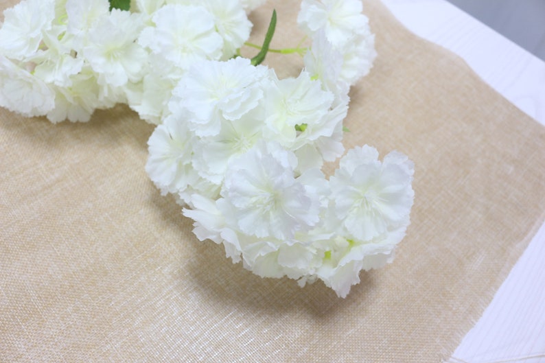 Pu&ograve; includere: Un mazzo di fiori artificiali bianchi con una texture delicata e a strati. I fiori sono disposti a cascata, creando un aspetto morbido e romantico.