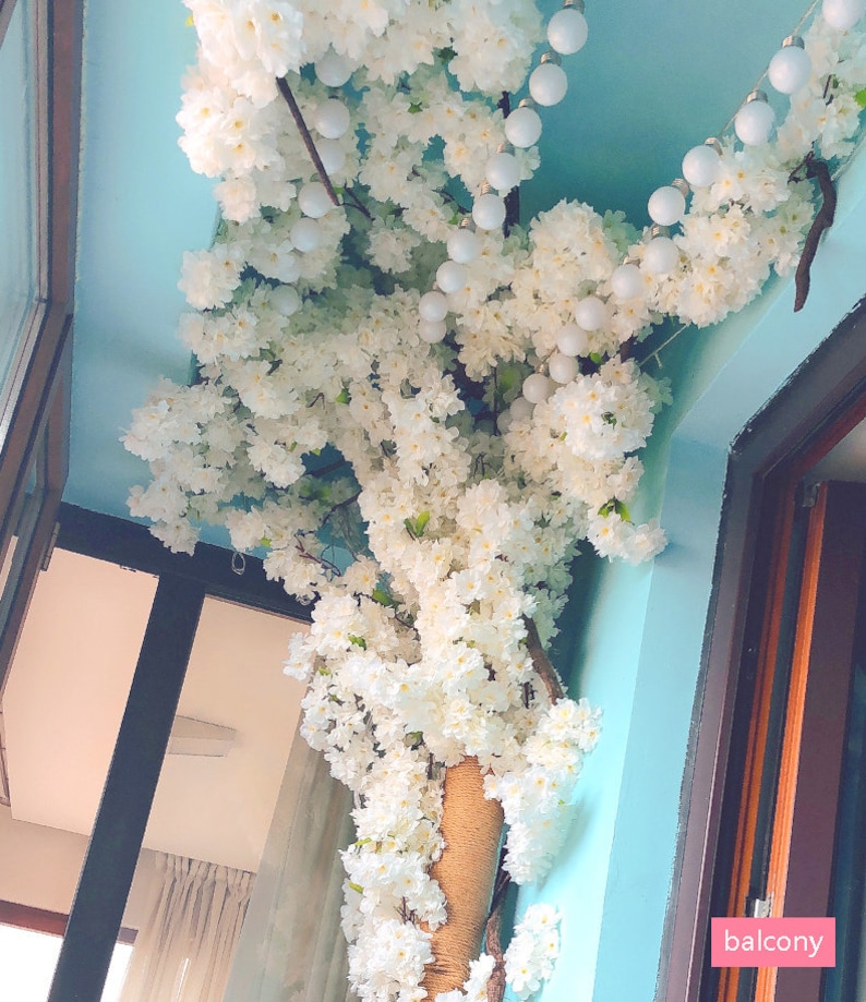 Pu&ograve; includere: Un'arrangiamento di fiori bianchi con luci bianche appese al soffitto. I fiori sono appesi al soffitto in un angolo di una stanza. La parola "balcone" &egrave; scritta in rosa su sfondo bianco nell'angolo in basso a destra dell'immagine.