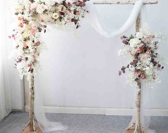 Pode incluir: Um arco de casamento de madeira de bétula branca decorado com flores artificiais brancas e rosas e vegetação. O arco é drapeado com tecido de tule branco.
