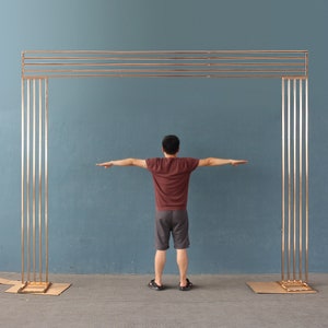 Puede incluir: Un arco de metal dorado con cinco barras horizontales y seis barras verticales. El arco está de pie sobre una superficie gris.