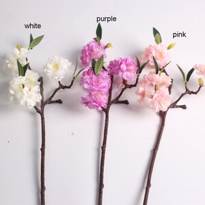 May include: Three artificial flower branches with white, pink, and purple blossoms. The branches are brown and have green leaves.