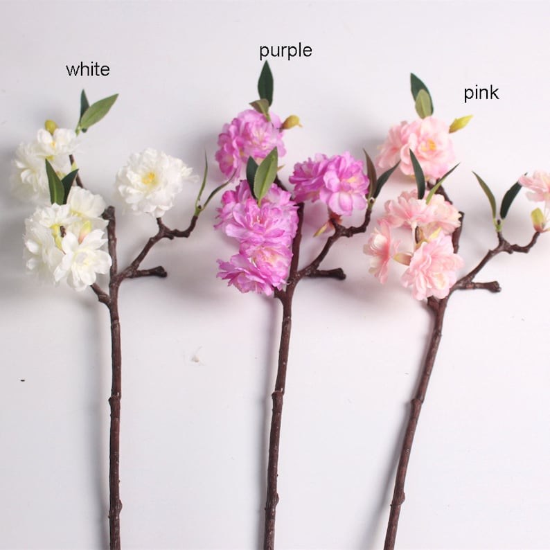 May include: Three artificial flower branches with white, pink, and purple blossoms. The branches are brown and have green leaves.