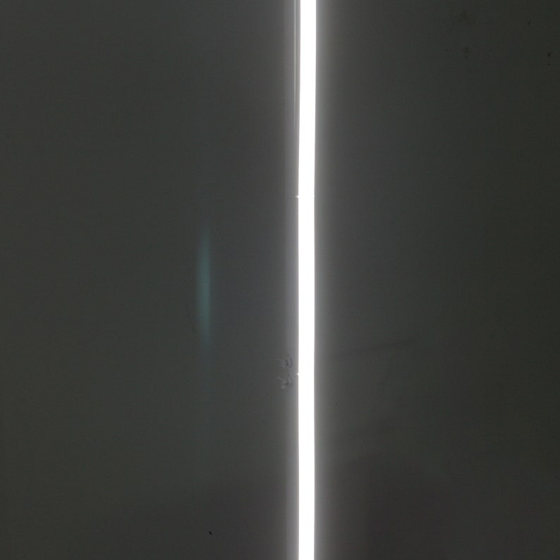 K&ouml;nnte beinhalten: Nahaufnahme einer wei&szlig;en vertikalen Lichtlinie vor einem dunkelgrauen Hintergrund.