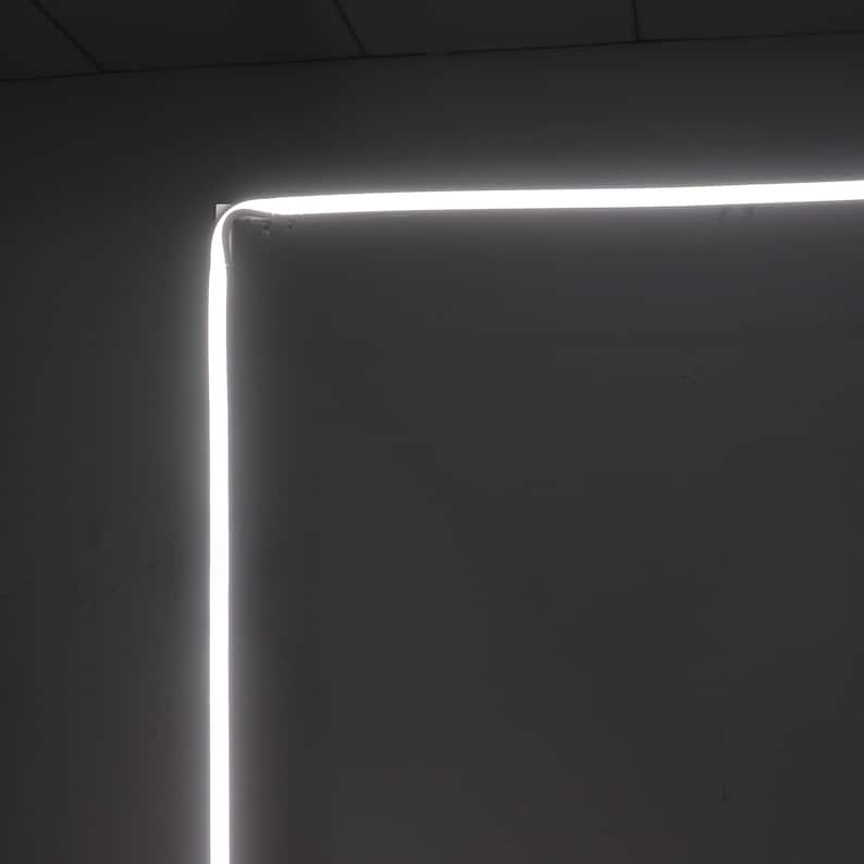 K&ouml;nnte beinhalten: Ein wei&szlig;er LED-Lichtstreifen ist an einer Wand montiert und bildet einen quadratischen Rahmen. Das Licht ist eingeschaltet und erzeugt einen hellen, wei&szlig;en Schein vor dunklem Hintergrund.