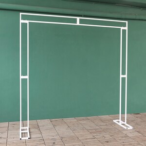 May include: White metal archway backdrop for a wedding or event. The archway is made of thin metal tubing and has a simple, modern design.