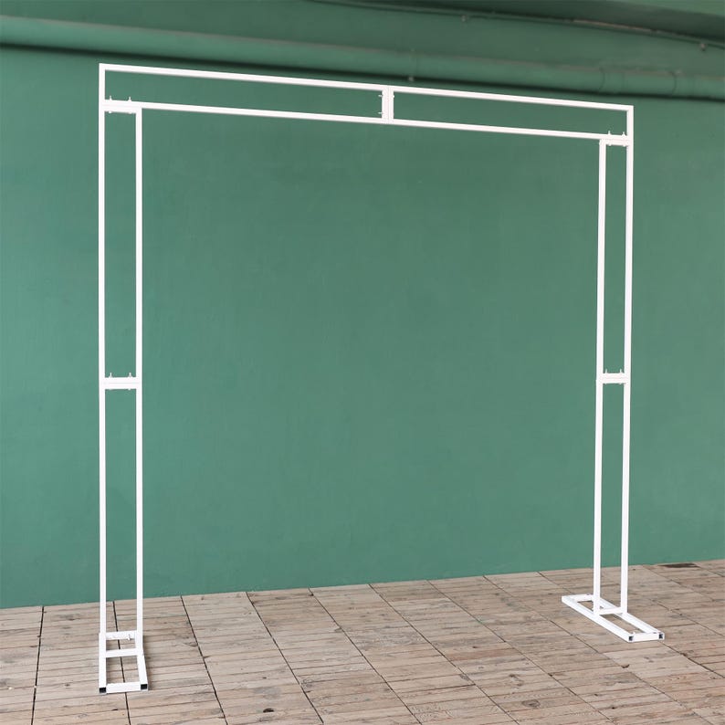May include: White metal archway backdrop for a wedding or event. The archway is made of thin metal tubing and has a simple, modern design.
