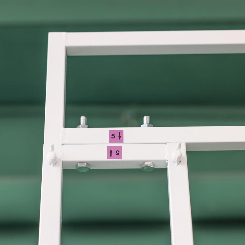 May include: Close-up of a white metal frame with two screws and pink labels that say "5" and "9" with arrows pointing up.