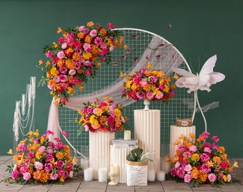 Pode incluir: Um arranjo floral vibrante com rosas rosa, laranja e amarelas, dispostas em pedestais brancos e um arco decorativo. A exibição inclui velas, um saco de papel com vegetação e uma grande decoração de borboleta.