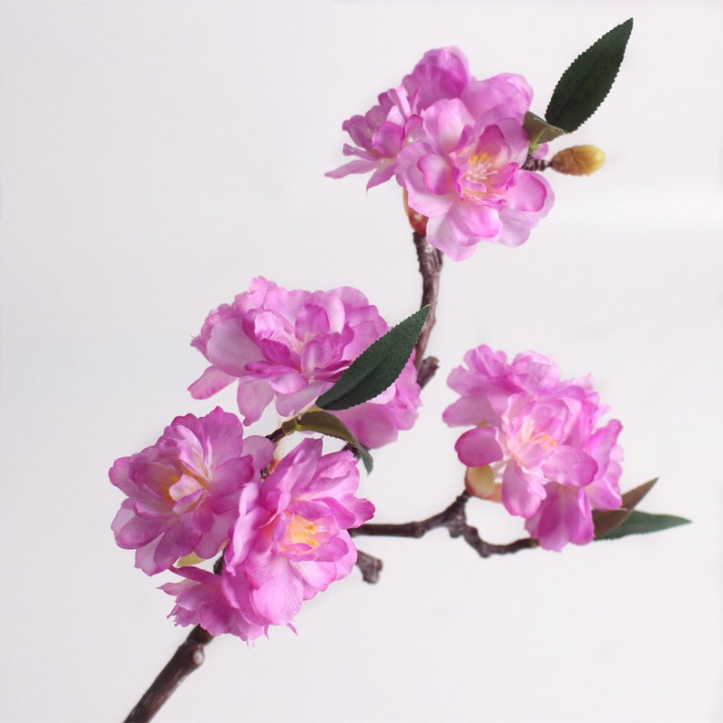 May include: A branch of artificial pink cherry blossoms with green leaves. The flowers are clustered together and have a delicate, realistic appearance.