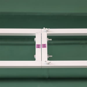 May include: A white metal frame with two bolts and wing nuts on each side. The frame has two pink labels with the numbers "61" and "69" on them.