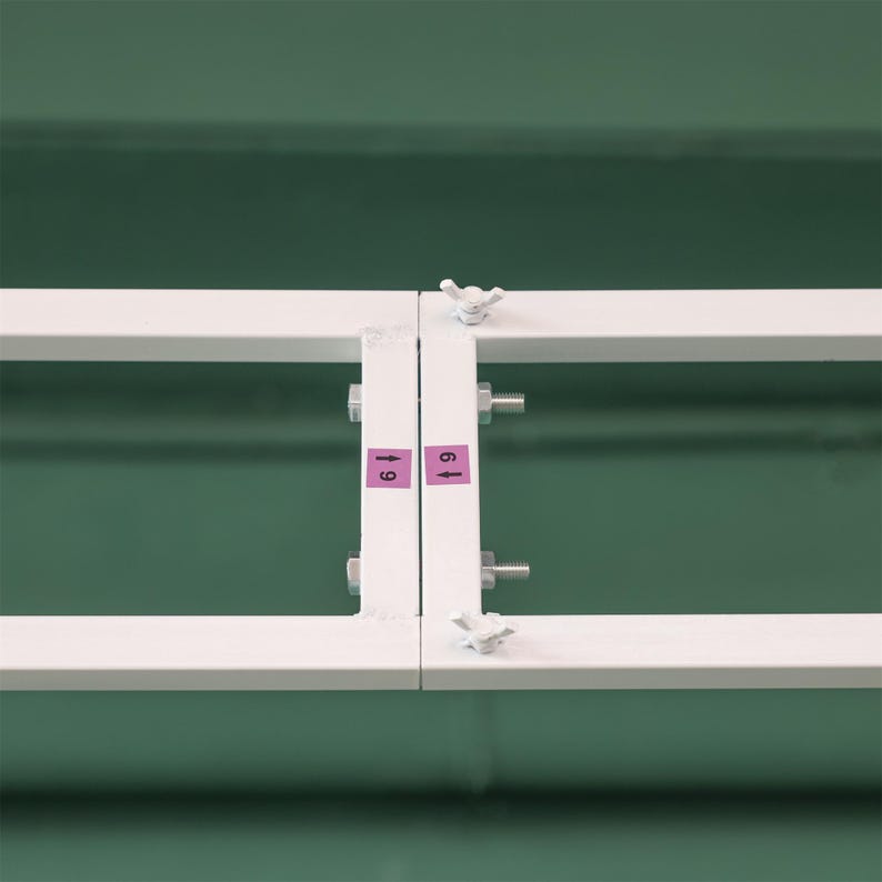 May include: A white metal frame with two bolts and wing nuts on each side. The frame has two pink labels with the numbers "61" and "69" on them.