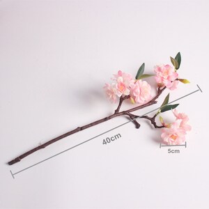 May include: A single branch of artificial pink cherry blossoms with green leaves. The branch is 40 cm long and the flowers are 5 cm wide.