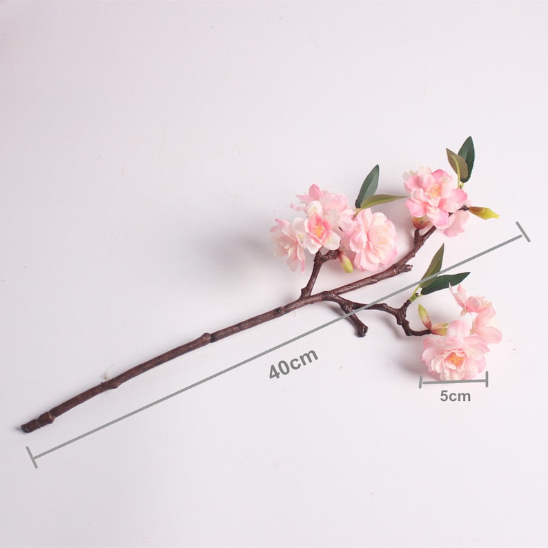 May include: A single branch of artificial pink cherry blossoms with green leaves. The branch is 40 cm long and the flowers are 5 cm wide.