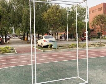 May include: White metal archway frame, standing on a red and green track surface. The frame is made of square tubing and has a rectangular shape.