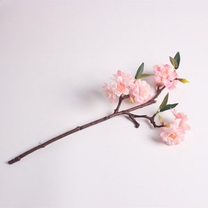 May include: A single stem of artificial pink cherry blossoms with green leaves. The stem is brown and the flowers are clustered together.