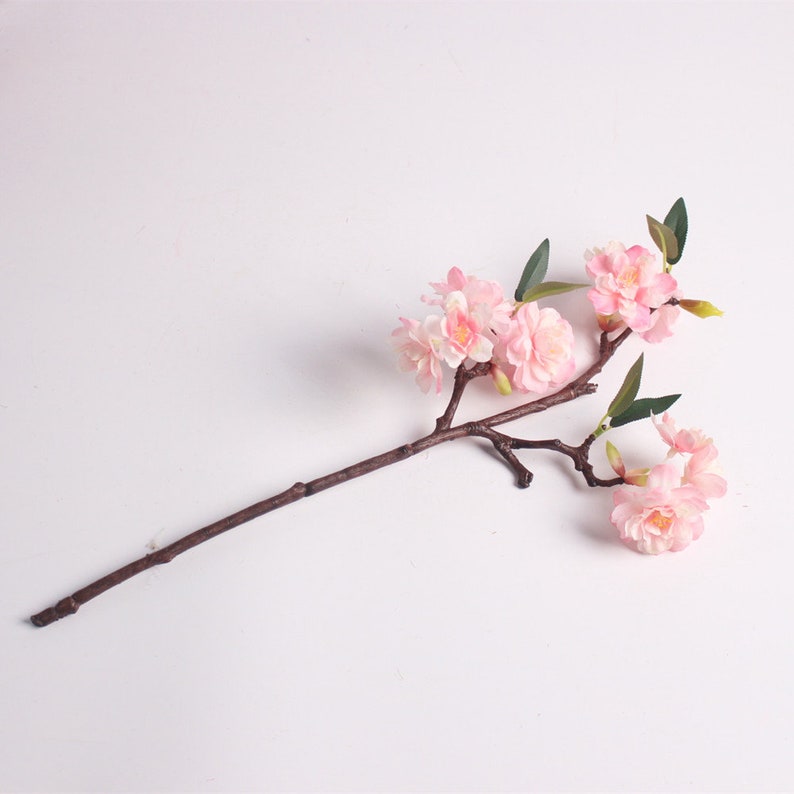 May include: A single stem of artificial pink cherry blossoms with green leaves. The stem is brown and the flowers are clustered together.