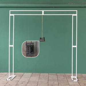 May include: White metal archway backdrop stand with two adjustable legs. A string hangs from the top of the archway with a weight attached to the end. The weight is a black metal block with the text "10KG" printed on it.