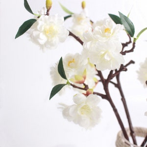 May include: A bouquet of white artificial cherry blossoms with green leaves on brown branches.