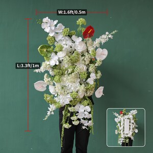 May include: A large floral arrangement featuring white orchids, roses, and anthuriums, accented with green foliage and a single red anthurium. The arrangement is approximately 3.3 feet (1 meter) tall and 1.6 feet (0.5 meters) wide.