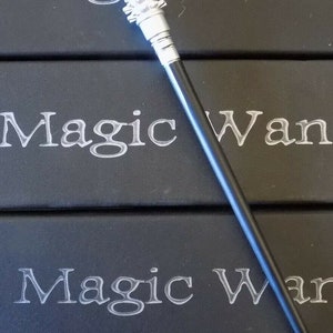 May include: A silver magic wand with a snake head design and a textured grip. The wand has a black handle and is displayed on a black surface with the words "Magic Wand" in white.