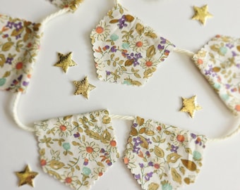 May include: A floral fabric banner with a cream-colored string, featuring small, gold-colored star-shaped embellishments scattered around. The banner's fabric has a white background with a pattern of small flowers in shades of purple, orange, and green.