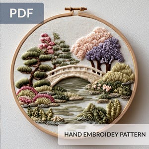 Puede incluir: Patrón de bordado a mano que representa un paisaje sereno con un puente, árboles y agua. El diseño utiliza hilos verdes, rosas y morados. Los textos "PDF" y "HAND EMBROIDEY PATTERN" son visibles.