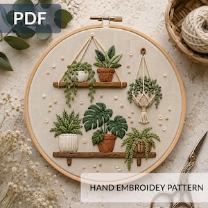 Könnte beinhalten: Ein runder Stickrahmen aus Holz mit einem Handstickmuster von verschiedenen Topfpflanzen auf Regalen und in einem Hängekorb. Das Design zeigt grünes Blattwerk, braune und weiße Töpfe sowie kleine verstreute Perlen auf einem beigen Stoffhintergrund.