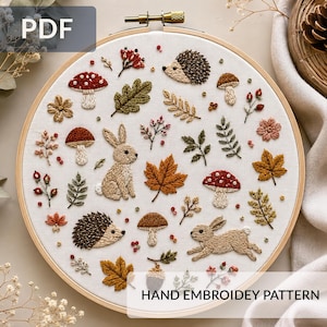 Könnte beinhalten: Ein handgesticktes Muster auf einem weißen Stoffreifen. Das Design zeigt Waldmotive wie Pilze, Blätter, Igel und Kaninchen in Braun-, Rot- und Grüntönen. Der Text "PDF" und "HAND EMBROIDERY PATTERN" sind sichtbar.