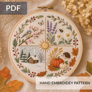 May include: A circular embroidery hoop featuring a four-season design on fabric. The quadrants depict spring with a bird and blossoms, summer with lavender and daisies, autumn with a pumpkin and hedgehog, and winter with a snowy cabin.