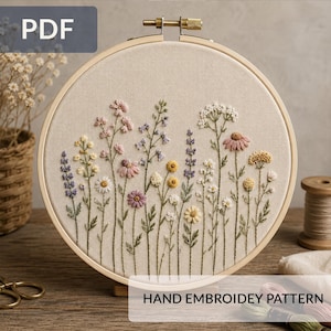 Puede incluir: Diseño floral bordado a mano sobre tela beige, tensado en un bastidor de madera. El diseño presenta varias flores silvestres en tonos rosa, amarillo, morado y blanco. El texto "HAND EMBROIDEY PATTERN" es visible.
