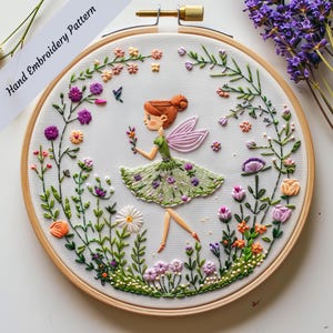 Puede incluir: Arte de bordado en aro con una hada con alas, un vestido verde y cabello castaño. El hada está rodeada de flores coloridas y vegetación.