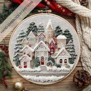 Puede incluir: Patrón de bordado a mano detallado de una escena de pueblo invernal, con casas cubiertas de nieve, árboles de hoja perenne y una iglesia. El bordado está en un aro de madera, con el texto "HAND EMBROIDERY PATTERN" visible. La paleta de colores incluye blanco, rojo y verde.
