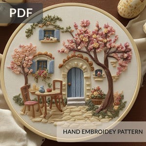 May include: A detailed hand embroidery pattern featuring a charming village scene. The design includes a blue door, windows with shutters, flowering trees, and a small table with chairs. The text "HAND EMBROIDERY PATTERN" is visible.
