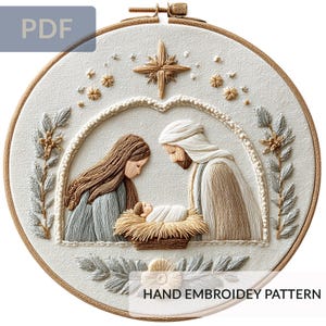 Peut inclure: Broderie sur cercle représentant une scène de la Nativité. Le motif comprend Marie, Joseph et l'enfant Jésus dans une mangeoire, avec une étoile au-dessus. L'œuvre est dans des tons beige, marron et bleu, avec le texte "HAND EMBROIDERY PATTERN".
