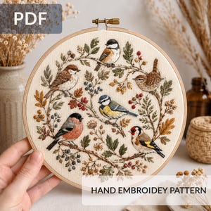 May include: A circular wooden embroidery hoop containing a cream-coloured fabric with a hand-stitched design of five birds perched on branches surrounded by leaves and berries. The text PDF and HAND EMBROIDEY PATTERN are visible on the image.