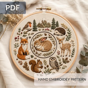 May include: A hand embroidery pattern in a wooden hoop, depicting a forest scene with a fox, rabbit, deer, and owl. The design includes trees, mountains, and foliage. Text reads "HAND EMBROIDERY PATTERN" and "PDF".