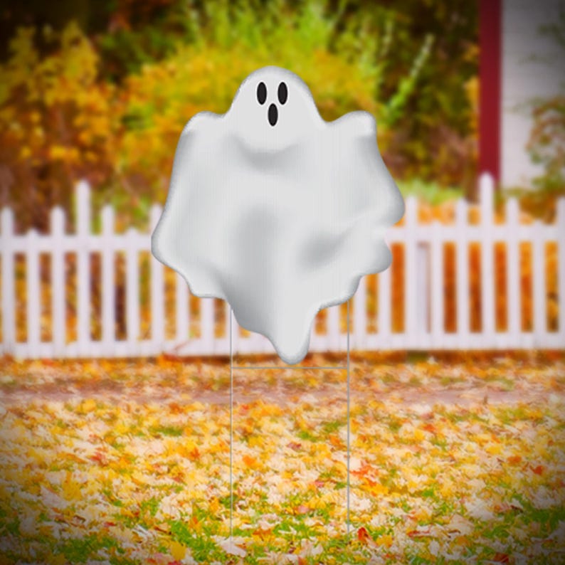 Pu&ograve; includere: Un cartello da giardino a forma di fantasma bianco con occhi neri e bocca. Il fantasma &egrave; in piedi su un paletto di metallo davanti a una staccionata bianca e uno sfondo di foglie autunnali.