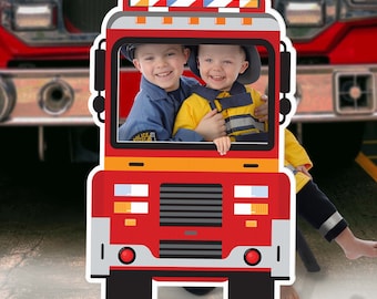 May include: Red and yellow cardboard cutout of a fire truck with two children's faces in the front window. The truck has a black grill and headlights. The children are wearing firefighter costumes.