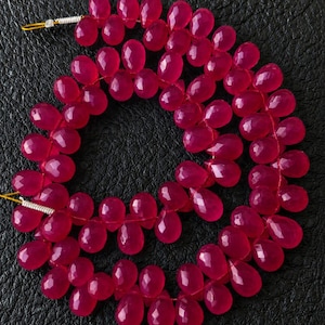 May include: A strand of faceted, teardrop-shaped beads in a vibrant magenta hue. The beads are strung together, creating a necklace-like arrangement. The beads are approximately 0.5 inches in length.