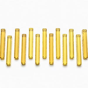 May include: A collection of fifteen rectangular glass bars in a vibrant yellow hue. Each piece features a smooth, translucent finish with rounded edges, arranged in a staggered, vertical row against a plain white background.