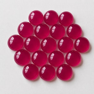 Peut inclure: Un ensemble de dix-sept cabochons circulaires, lisses et translucides d'une couleur rose magenta vibrante. Chaque pièce présente une surface supérieure bombée avec une finition brillante qui reflète la lumière, disposée en grappe.