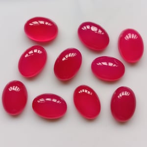 May include: Ten oval-shaped, pink gemstones with a glossy finish. The stones are arranged in a scattered pattern on a white surface.