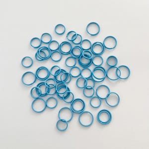 May include: A large group of blue metal rings scattered on a white surface.