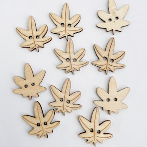 May include: Ten wooden buttons shaped like maple leaves with two holes each. The buttons are light brown and have a natural wood finish.