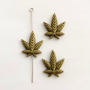 May include: Three gold-colored marijuana leaf charms with a silver wire loop. The charms are perfect for jewelry making or adding a touch of whimsy to your crafts.