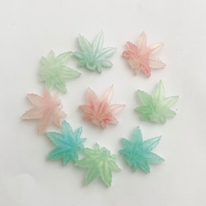May include: A collection of nine resin leaf charms in various shades of green and pink. The leaves are translucent and have a glittery finish.