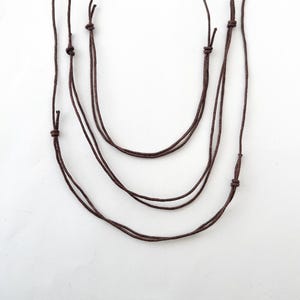 May include: Three brown cords tied together in a series of knots, creating a layered necklace effect.