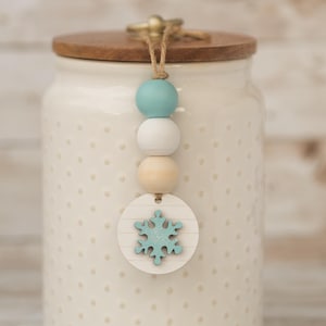 May include: White ceramic jar with a wooden lid and a blue and white snowflake charm hanging from the lid. The jar has a white polka dot pattern.